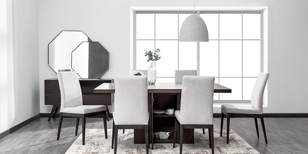 Comedor con mesa oscura y sillas tapizadas en gris claro, frente a un ventanal y espejos octagonales