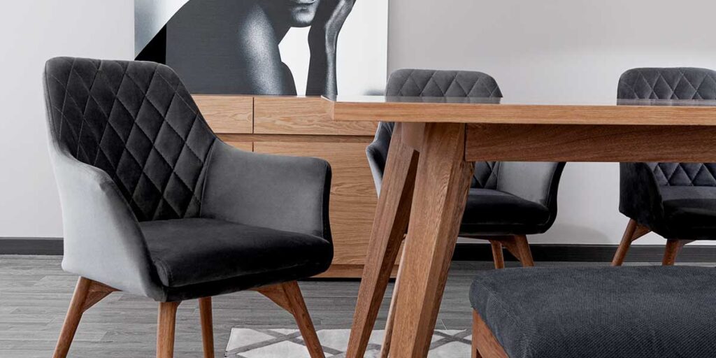 Detalle de una silla de terciopelo gris oscuro con capitoné de rombos junto a una mesa de comedor de madera