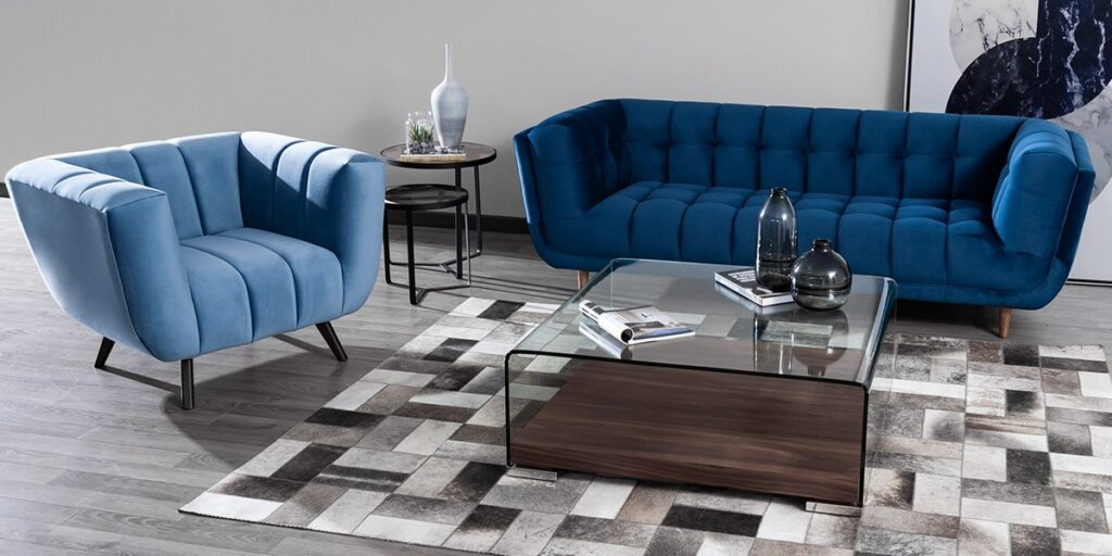 Sofá azul oscuro capitoneado y butaca azul de canales con mesa de centro de vidrio y madera sobre un tapete de patchwork gris